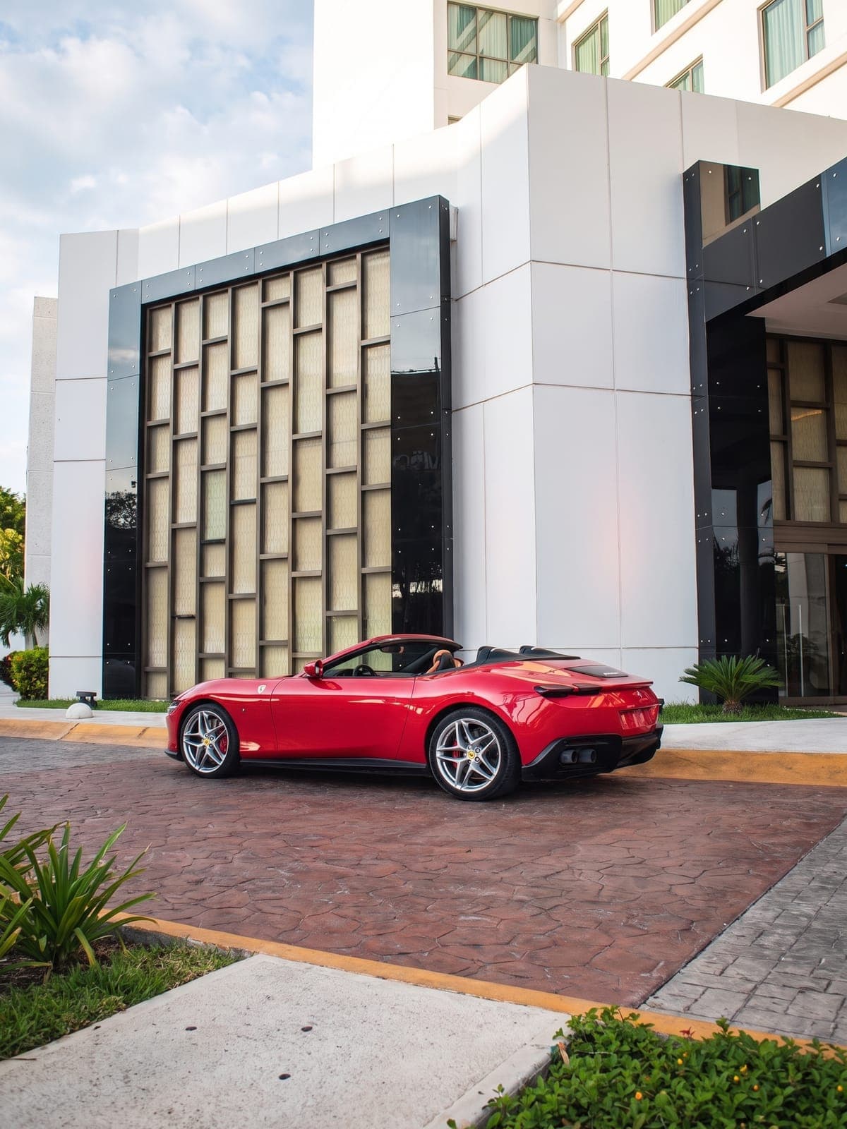 Ferrari Roma rojo estacionado frente a un edificio de líneas modernas.