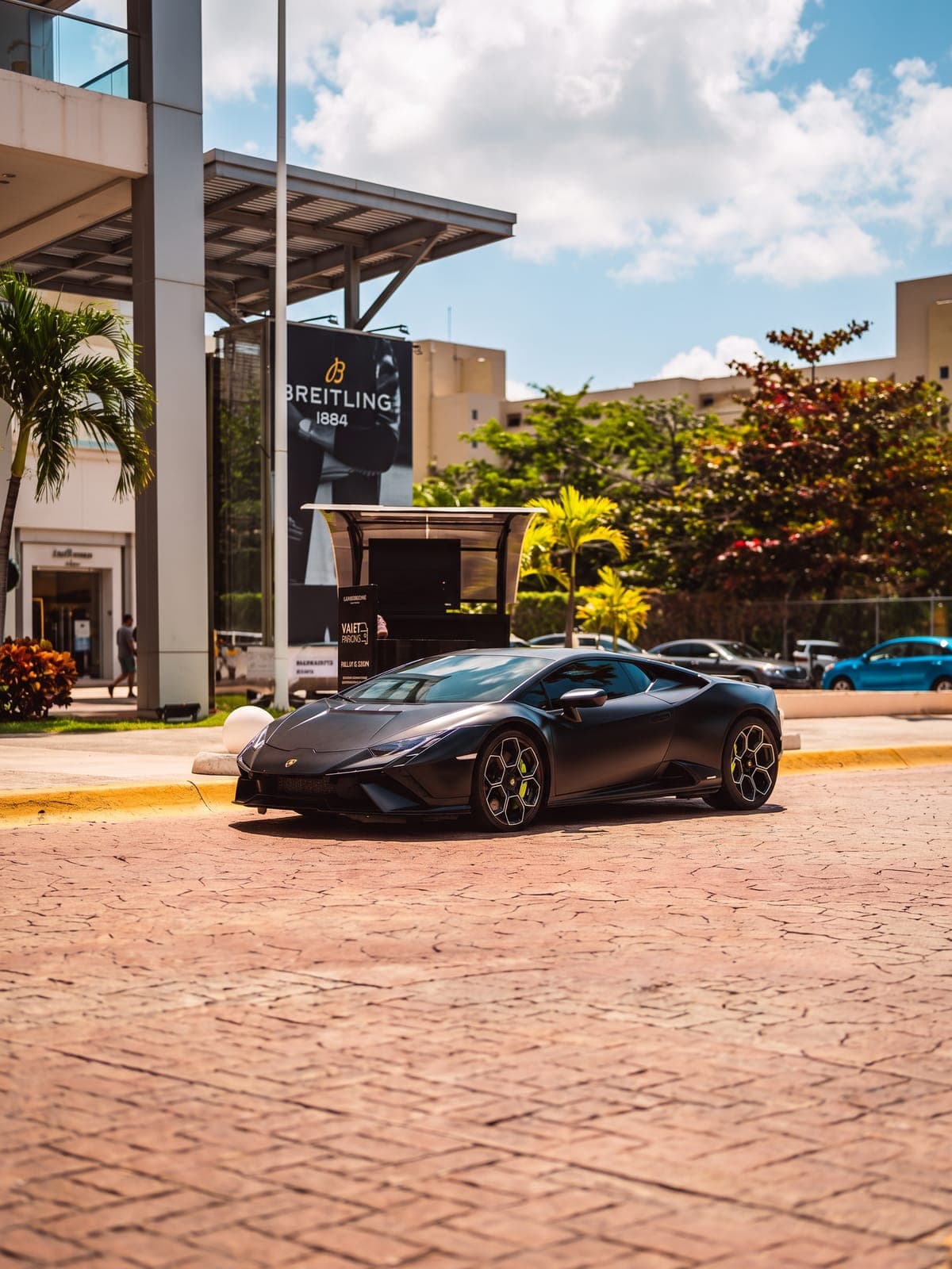 Lamborghini Huracán negro mate en una plaza con palmeras.