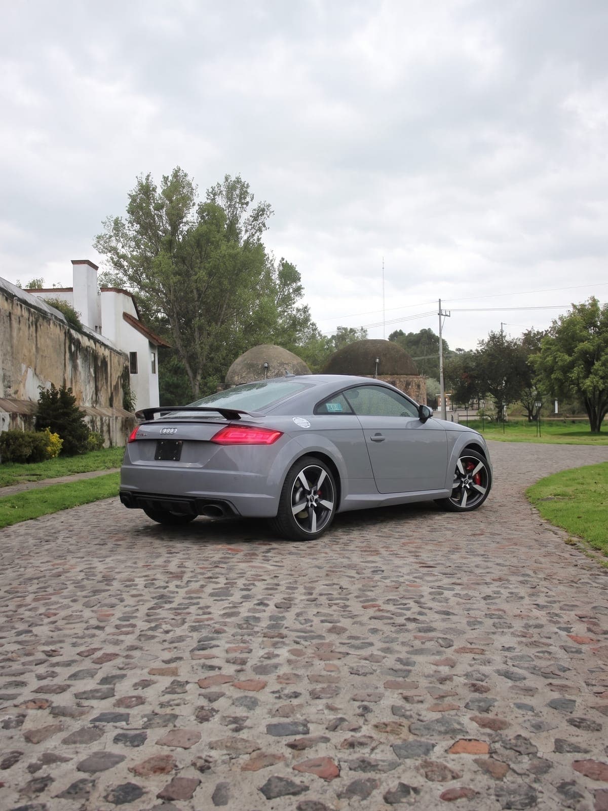 Audi TT RS gris frente a un muro de piedra de una hacienda.