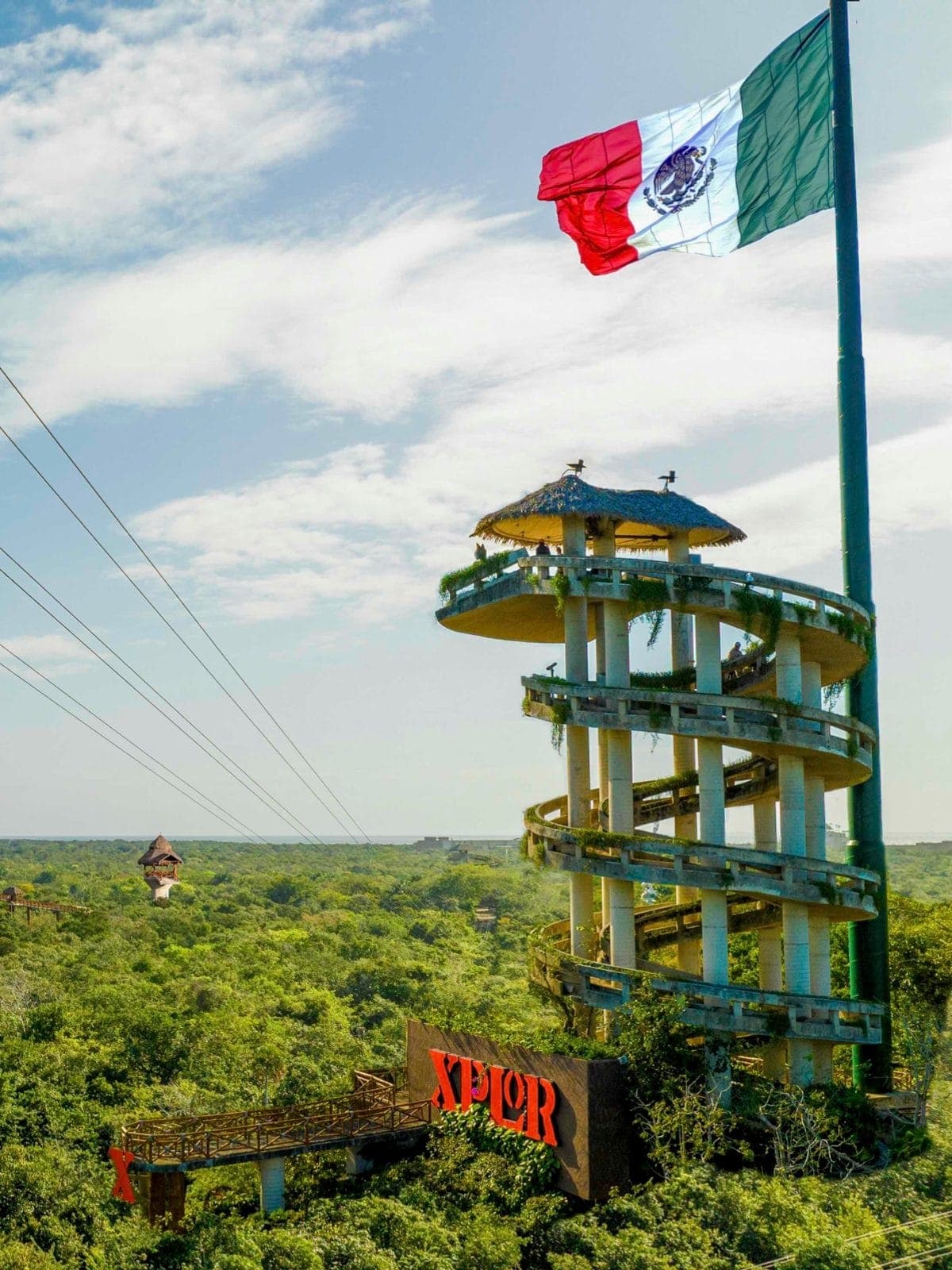 Torre de un parque de aventura con la bandera de México sobre la selva.