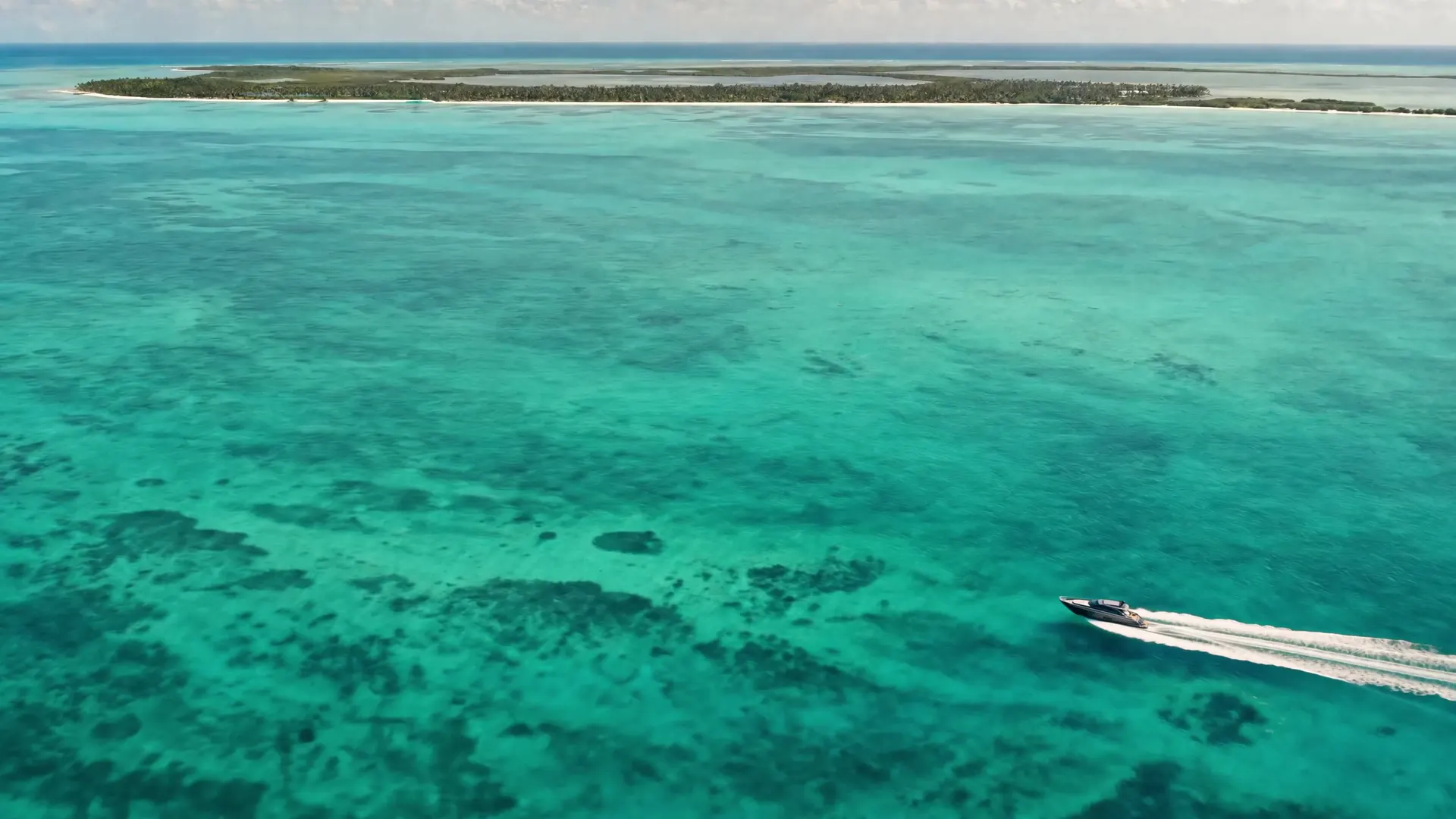 Yate de casco negro navegando sobre el Caribe turquesa frente a una isla de arena y palmas.