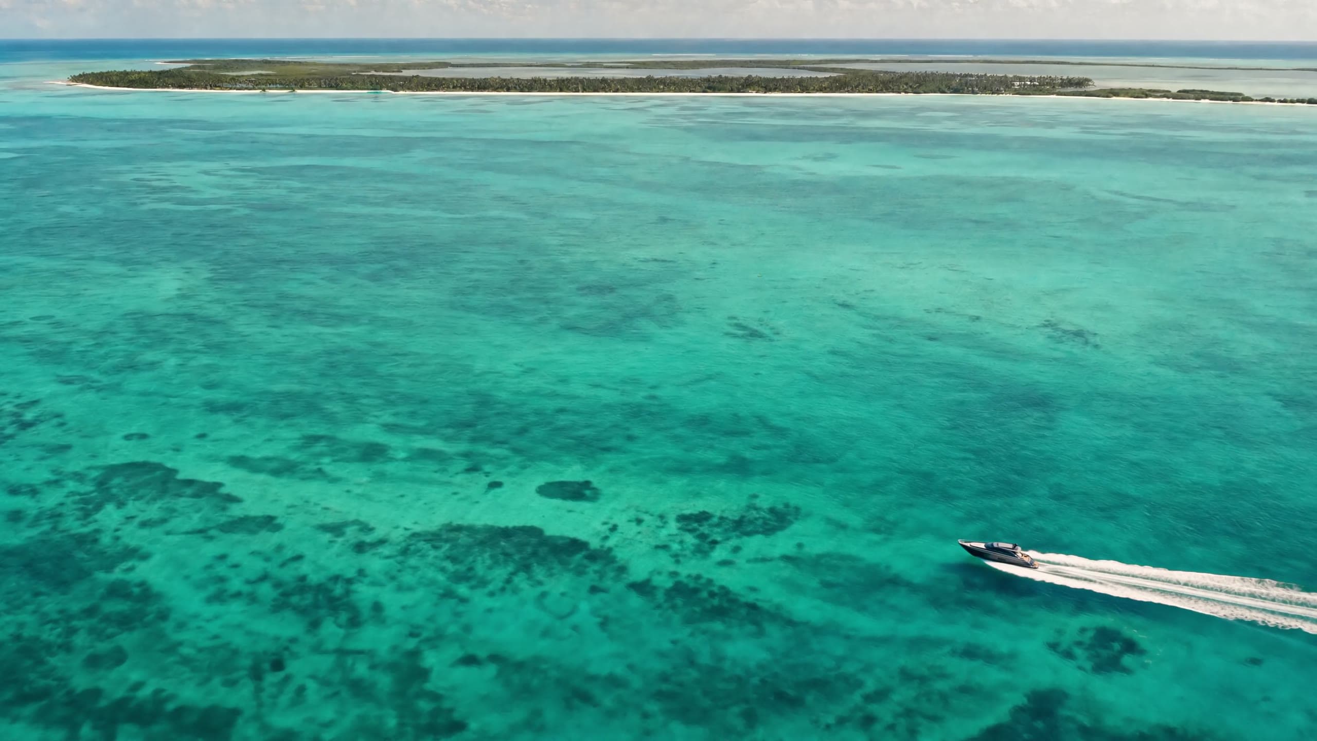 Yate de casco negro navegando sobre el Caribe turquesa frente a una isla de arena y palmas.
