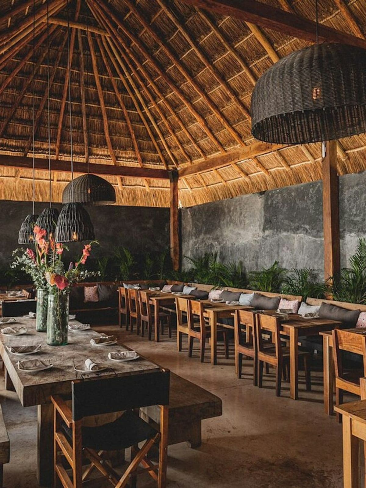Gitano, mezcal y cocina en Tulum: palapa con lámparas de ratán y mesa comunal con flores.