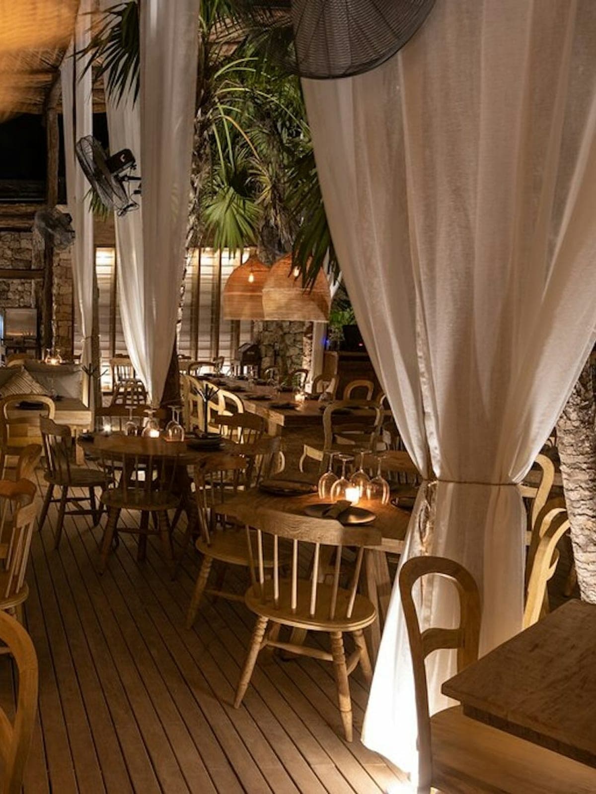 Chambao, restaurante de playa en Tulum: interior con cortinas blancas y velas junto al mar.