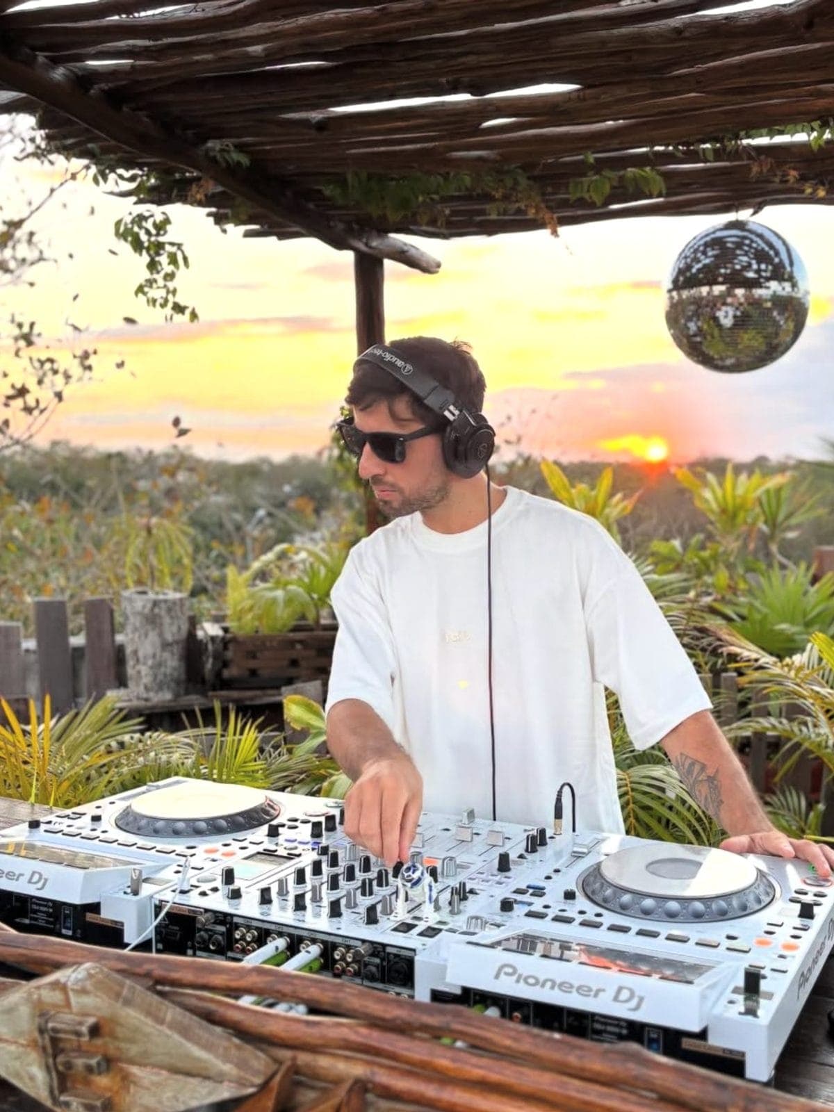 DJ tocando bajo una palapa al atardecer.