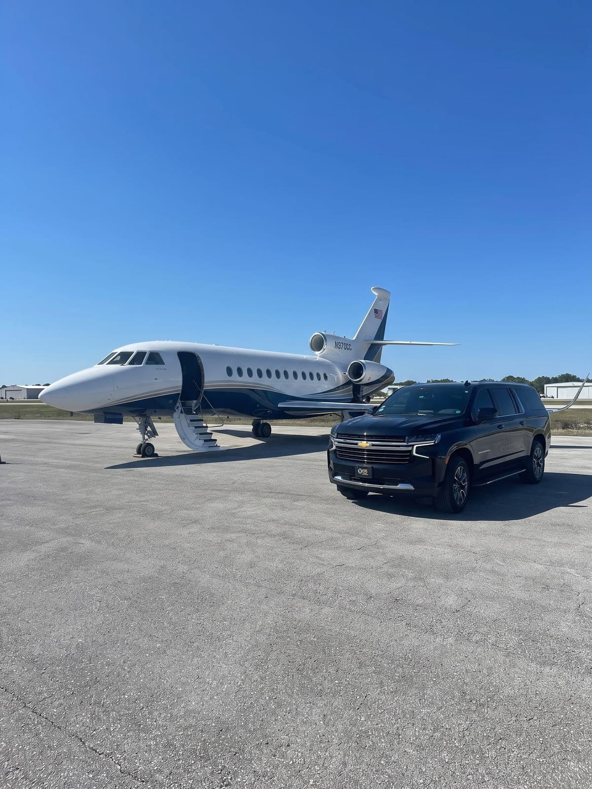 Camioneta Suburban negra junto a un jet privado en la plataforma.
