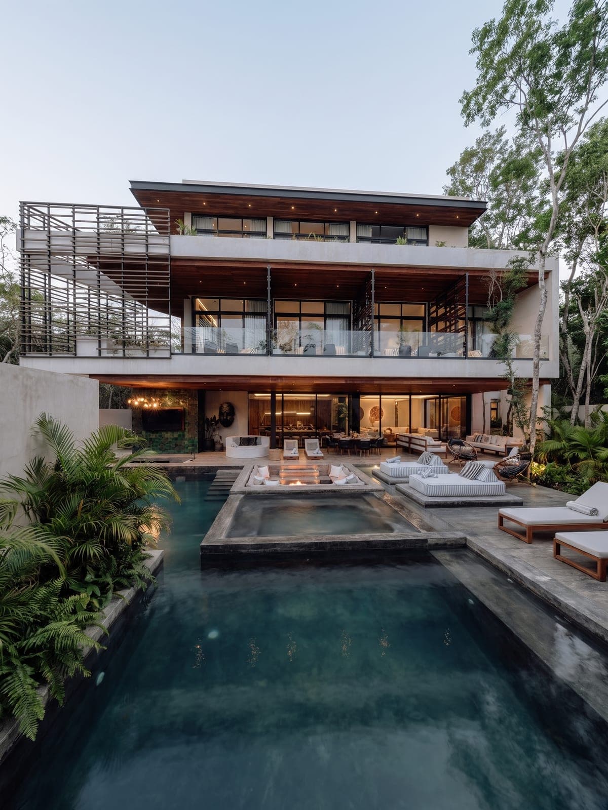 Casa Luna, a design home in Tulum, Riviera Maya: an open wood-and-concrete living room with a pool and fire pit at dusk.