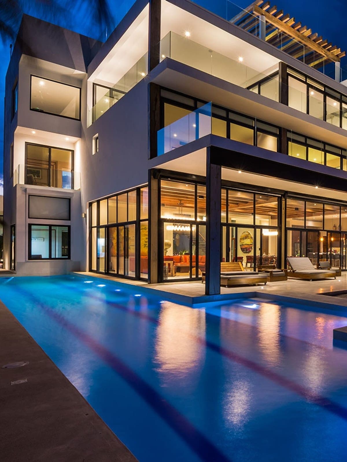 Napa, a design home in Tulum, Riviera Maya: a lit glass villa with a blue pool at dusk.