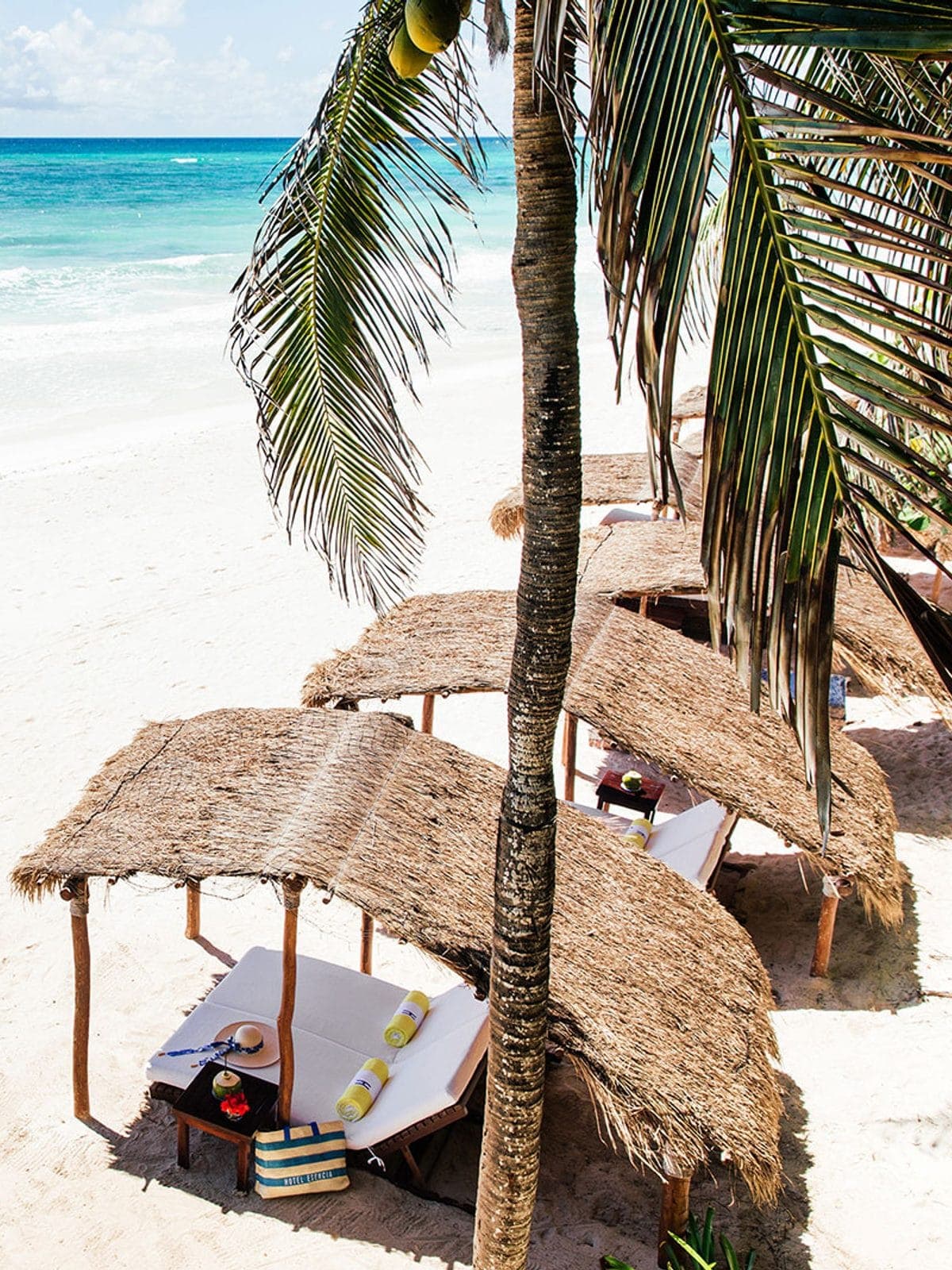 Palapa de playa sobre la arena junto al agua turquesa.