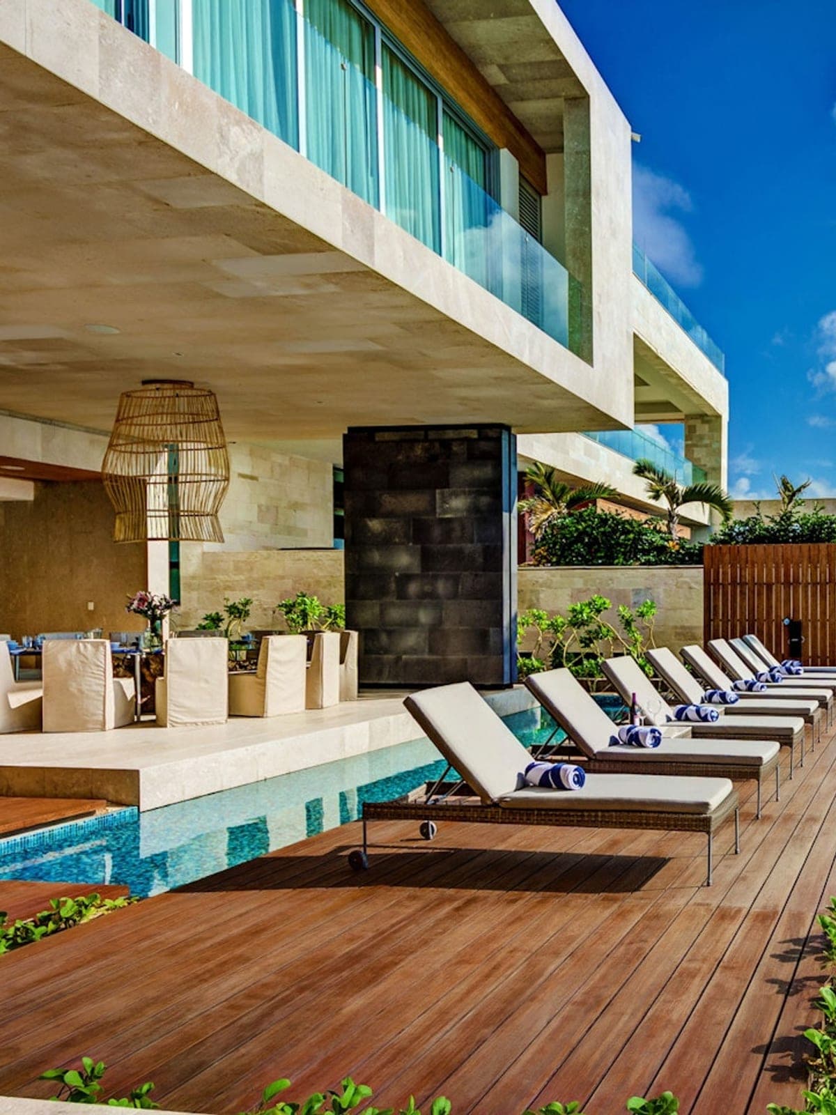 Kin Ich, a design home in Playa del Carmen, Riviera Maya: a glass villa with a long pool and loungers among palm trees.