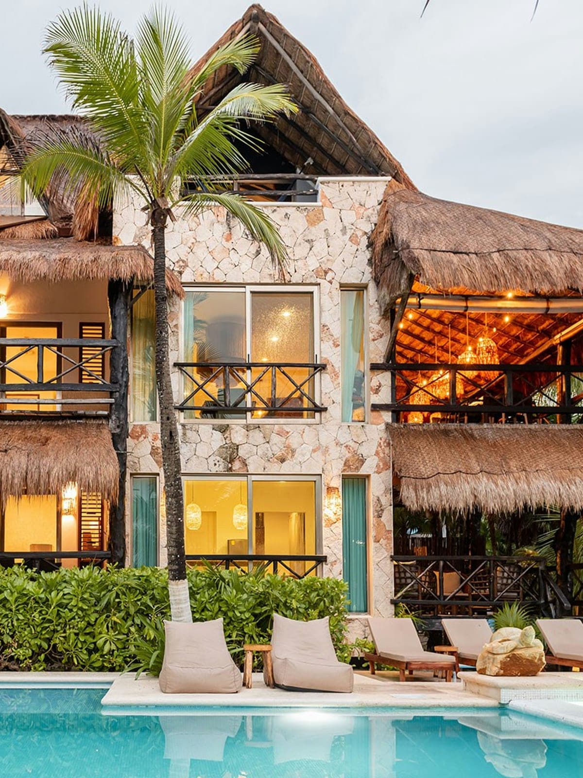 Sombras del Viento, a palapa house in Tulum, Riviera Maya: a villa lit at dusk among palm trees.