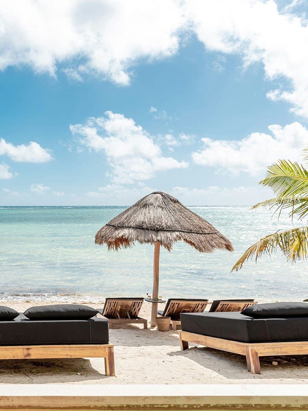 Zama, an oceanfront villa in Tulum, Riviera Maya: a palapa and loungers on the sand facing turquoise water.