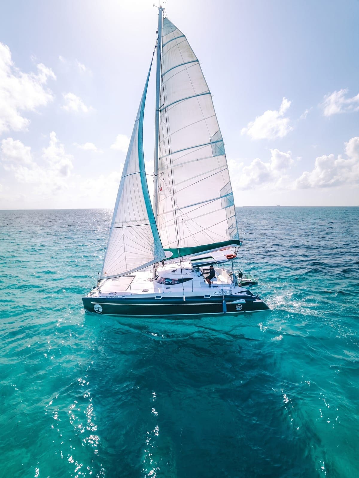 Catamarán de vela fondeado sobre agua turquesa.